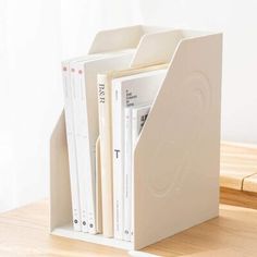 a white book holder with three books in it on top of a wooden table next to a laptop