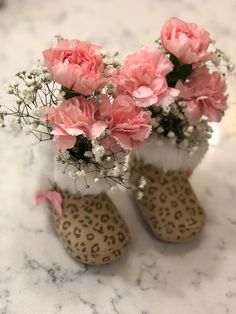 some pink flowers are sitting in boots on a marble counter top with leopard print slippers