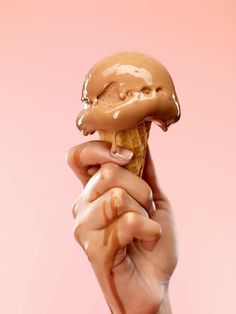 a person holding an ice cream cone in their hand with chocolate icing on it