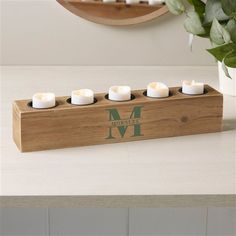 a wooden welcome home candle holder with six lit candles in front of a mirror and potted plant