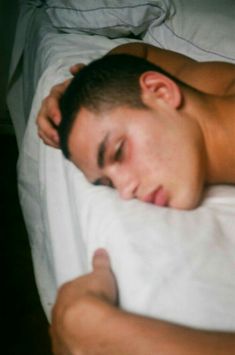 a young man sleeping on top of a white bed next to a hand pointing at the pillow