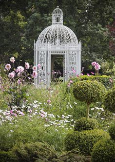 a white gazebo surrounded by lots of flowers and bushes in the middle of a garden