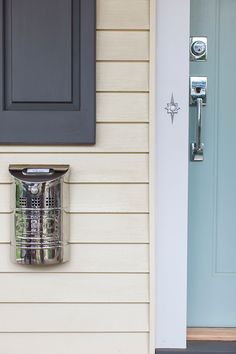 a metal trash can sitting on the side of a house next to a blue door