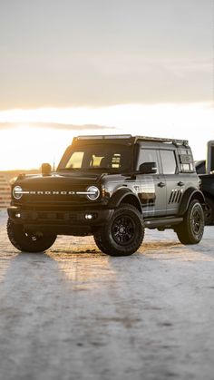 two jeeps parked next to each other in a parking lot with the sun setting behind them