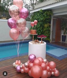 some pink and gold balloons are on the ground near a pool with a cake in it