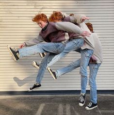 three people are jumping in the air with their arms around each other and one person is wearing jeans