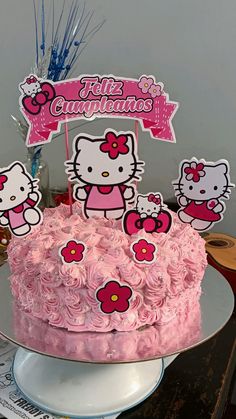 a hello kitty birthday cake with pink frosting and decorations on the top, sitting on a table