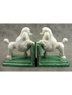 two white poodle figurines sitting on top of green bookends in front of a gray background