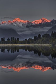 the mountains are covered in clouds and reflecting in the still water at sunset or dawn