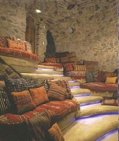 a room filled with lots of pillows on top of floor next to stone walls and windows