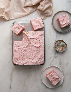 pink frosted cake with sprinkles sitting on a table next to two plates