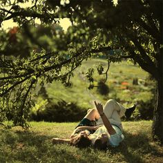 two people laying in the grass under a tree with their hands up to each other