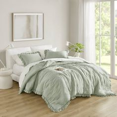 a bedroom with white walls and wooden flooring has a green comforter on the bed