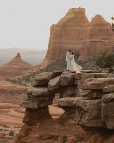 a bride and groom standing on top of a rock formation in front of the desert