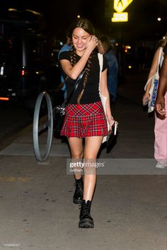 a woman walking down the street talking on her cell phone while wearing a plaid skirt