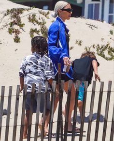 a woman and two children are walking on the sand near a fence at the beach