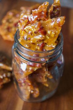 a glass jar filled with food sitting on top of a wooden table next to crackers