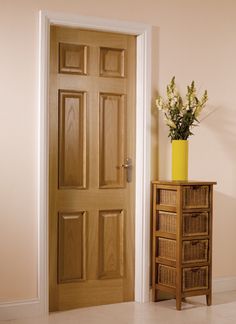 a vase with flowers sitting on top of a wooden table next to a door that is open