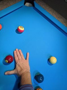 a person is reaching for balls on a pool table with blue felt and yellow rubber balls