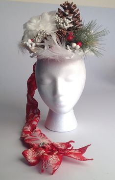 This hat is truly a wintery vignette that will make you feel like you in the snowy woods!  Snowy white woodsy pinecones, large white feather ball are set upon a green and white striped fabric with gold dots.  Adorned with a small gold and larger red and white berries and snow powdered twigs.  The rim of the hat is circled with white feathers creating a flowing soft movement.  Further embellished with a pine tree limb adds more color and texture.  The bottom of the hat is red with silvery swirls.  It is approximately 8 inches circular with a sturdy headband for stylish comfortable ease of wear.  Weighing in at less than 8 ounces, you can wear this for hours.  Two bows and my signature ribbon braid made from a red ribbon with white twigs and gold sparkles beautify the back of the hat for a c Snowy Pinecone, Diy Hats, Christmas Pine Tree, Styrofoam Head, Snowy Woods, Ribbon Braids, White Berries, Christmas Hats, Winter Schnee