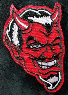 a red devil with horns and fangs on it's face is embroidered onto a black jacket