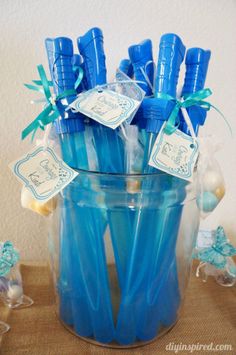 blue toothbrushes are in a clear glass container with tags on them for favors