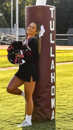 a cheerleader posing in front of a tall sign on the side of a field