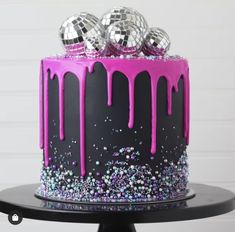 a black and pink cake with purple icing on top, topped with disco balls