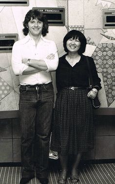 two people standing next to each other in front of a wall