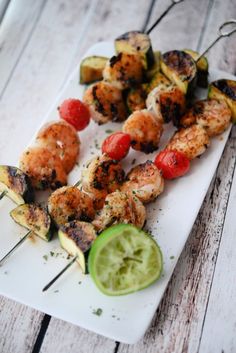 grilled shrimp and vegetable skewers on a white plate with a cucumber