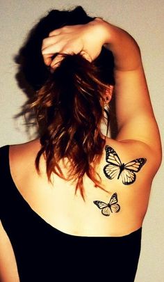 a woman with two butterflies on her upper arm and shoulder, behind her is a white wall