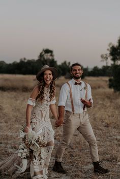 a man and woman are walking through the field holding hands with each other while wearing suspenders