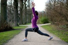 a woman in purple shirt doing yoga on dirt road with trees and grass behind her