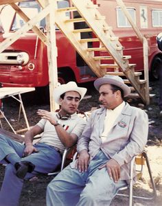 two men sitting next to each other in chairs near a firetruck and truck