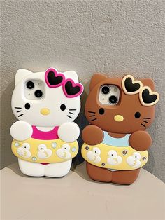 two hello kitty phone cases sitting on top of a table next to each other,