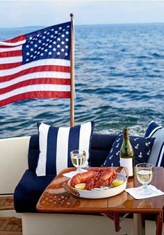 a plate of lobsters on a wooden table next to the ocean and an american flag