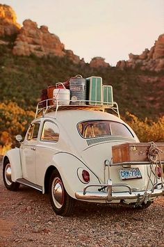 an old vw bug with luggage on top parked in front of a mountain range