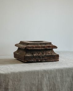 an old wooden object sitting on top of a white cloth covered tablecloth in front of a gray wall