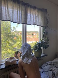 a naked man sitting in front of a window next to a potted plant