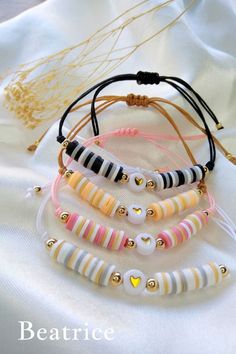 four bracelets with different colors and designs on white fabric, one has gold beads