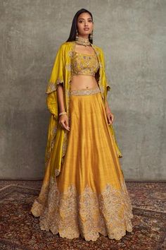 Mustard asymmetric &cutwork cape with floral embroidered motifs. Paired with floral embroidered scallop lehenga and embroidered bustier.
Component: 3
Pattern: Embroidered
Type Of Work: Floral
Neckline: Open
Sleeve Type: Flared Sleeves
Fabric: Raw Silk
Color: Yellow
Other Details: 
Scallop hem lehenga
Floral motifs
Tassel detail
Asymmetric cape
Occasion: Bride, Sangeet - Aza Fashions Ruffled Saree, Pink Sharara, Latest Lehenga Designs, Cape Lehenga, Diwali Dresses, Minimalistic Outfits, Jayanti Reddy, Raw Silk Lehenga, Yellow Lehenga