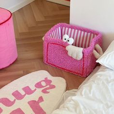 two stuffed animals sitting in pink baskets on the floor next to a bed with white sheets and pillows