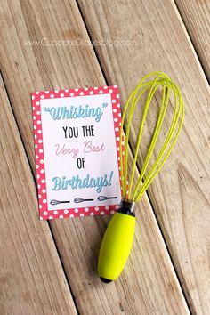 a yellow whisk sitting on top of a wooden table next to a sign