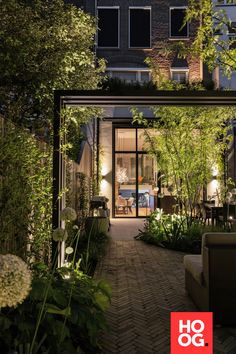 an outdoor living area is lit up at night, with plants and flowers in the foreground