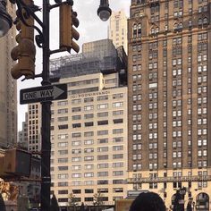 people are standing on the street corner in front of tall buildings and traffic lights with one way signs