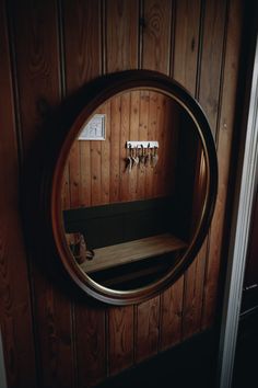 a circular mirror hanging on the side of a wooden wall next to a coat rack