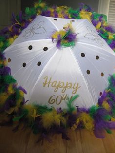 a white umbrella with purple, yellow and green feathers on it that says happy 60th