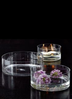 three glass bowls with flowers in them sitting on a table next to a lit candle