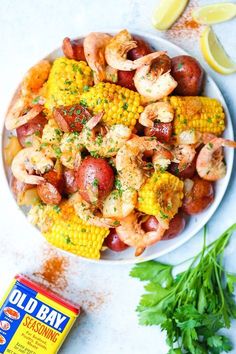 a white plate topped with shrimp, corn and potatoes next to a can of old bay seasoning