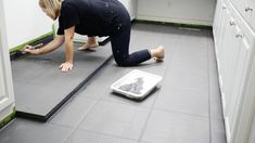 a woman kneeling down on the floor in front of a kitchen counter with a scale